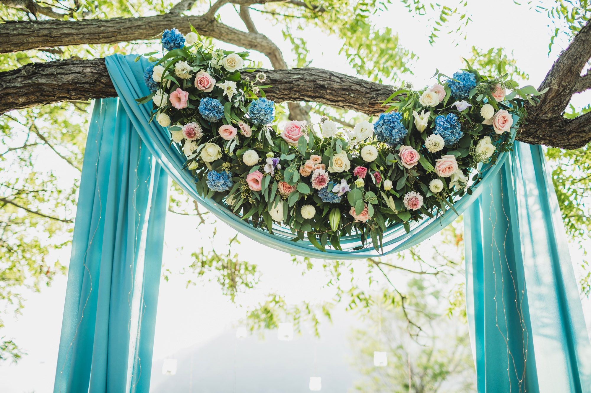 Sunset wedding ceremony arch with flower decoration and blue cloth canopy hanging on big tree